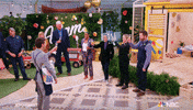 Reality TV gif. Camera pans around the set of Making It, where contestants and hosts raises their glasses to cheers and clap their hands.