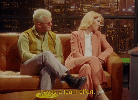 Celebrity gif. Music duo Broods is being interviewed and they sit on a couch with their legs crossed. They nod and smile as they say, "It was a team effort."