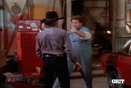 TV gif. A man wearing a light blue jumpsuit punches Chuck Norris as Ranger Cordell Walker in Walker, Texas Ranger, sending him spinning. Walker then backhands the man and he stumbles into a red car.
