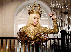 Celebrity gif. Nicki Minaj all in gold with a sequined dress and majestic crown, striking a pose.