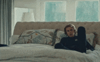 Music video gif. The Kid Laroi in the Selfish Music video lounges on a bed as he sings, “I’m grateful for what you did for me.”