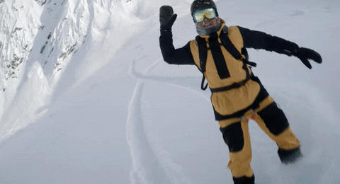 Video gif. On a snowy mountain, a smiling snowboarder in yellow and black snow gear with a gopro on his helmet gives us a high five with his mittened hand.