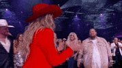 ACM Awards gif. Country music artist Lainey Wilson with a smile on her face claps while walking up like an old friend to Jelly Roll to give him a hug and as they seperate one of his hands linger on her forearm before he walks away completely. 