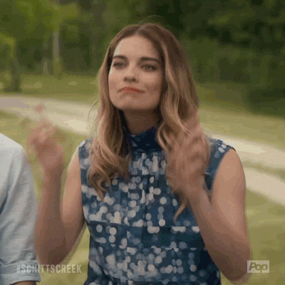 Schitt's Creek gif. Annie Murphy as Alexis crosses her fingers with both hands as she smiles earnestly before looking down. 