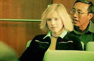 TV gif. Kristen Bell as Veronica in Veronica Mars. She sits in the audience and cheekily gives us a wink and a finger gun.