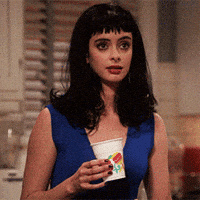 TV gif. Krysten Ritter as Chloe on Don’t Trust the B in Apartment 23 holds a plastic cup in her hand. She lights up in excitement, her eyes getting big and her mouth opening wide into a big smile.