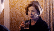 Arrested Development gif. Jessica Walter as Lucille Bluth starkly winks one eye, her lips pursed as she raises a glass of whisky.