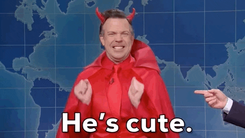 SNL gif. Jason Sudeikis is dressed as a devil and is in front of the SNL newscasting board. He uses his hands to air squeeze while also scrunching his shoulders and expression together for emphasis and says, "He's cute!"