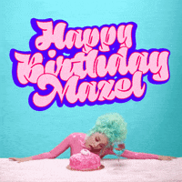 Celebrity gif. Doja Cat sporting a bright aqua beehive, licks a pink cake on a table in front of her, a goldfish in a wineglass beside, big graffiti-style letters bounce and bob above her, reading "Happy birthday, mazel."