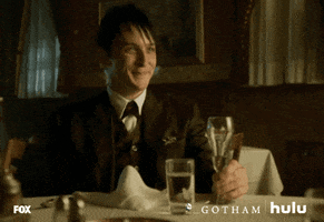 TV gif. Robin Lord Taylor as Oswald Cobblepot in Gotham smiles and raises his glass to cheers.