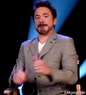 Movie gif. Robert Downey Jr. sits in a director's chair wearing a gray blazer. We zoom out slightly as he gives us an understated double thumbs up.