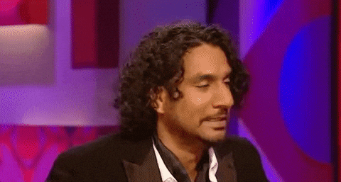 Celebrity gif. Naveen Andrews flips his hair back with casual sass.