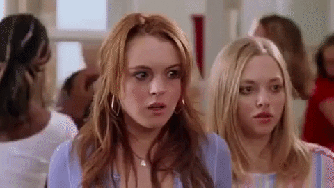 Movie gif. Lindsay Lohan as Cady and Amanda Seyfried as Karen in "Mean Girls" back up nervously as classmates scurry and stampede around them.