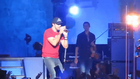 Celebrity gif. Luke Bryan is singing onstage at his concert and he suddenly hits a deep body roll, feeling himself.