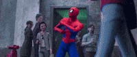 Video game gif. Spider-Man dances, shaking his hips and twirling his wrists around each other, as people walk in and out of a doorway glancing at him.