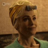 TV gif. Gemma Arterton as Barbara Parker on Funny Woman. She's wearing a yellow head wrap and a curler. She has a green sweater on and she splutters out laughing, covering her mouth at the last minute. 