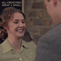 TV gif. Anna Madeley as Mrs. Hall in All Creatures Great and Small beams as she reaches up and kisses a man. 