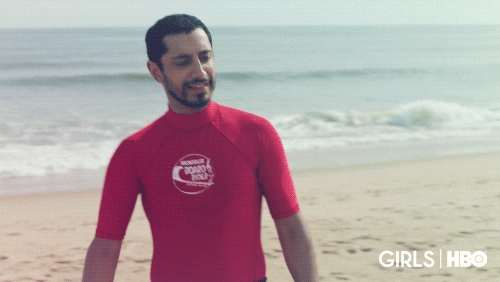 TV gif. Riz Ahmed as Paul-Louis from Girls wears a red rash guard at the beach as he leans back and puts up his hands up, sarcastically surrendering to something that doesn't actually faze him.