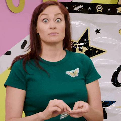 Video gif. Mamrie Hart from "This Might Get" fiddles with something in her hands and nods emphatically, wide-eyed.