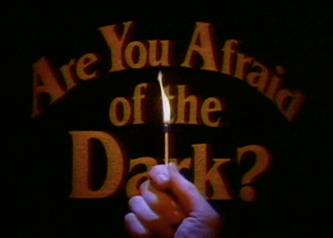 Text gif. Written in a haunting orange font, text reads "Are You Afraid of the Dark?" while a hand holds a singular burning match in front.