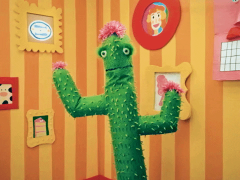 TV gif. A cactus puppet in Happy Place raises its arms bobbing as it speaks with a friendly expression in a room with bright cartoonish decor. Text, "Hang in there friend!'