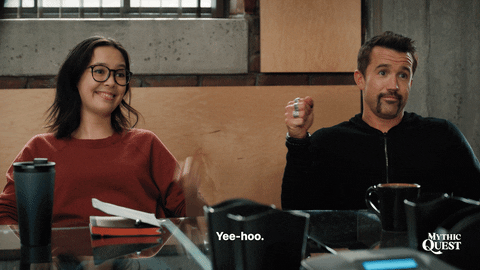 TV gif. Charlotte Nicdao and Rob McElhenney as Poppy and Ian in Mythic Quest blindly fist bump in sync. Text, "yee-hoo."