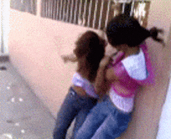 Video gif. Two teenage girls fight, grabbing onto each other’s hair and shirts.