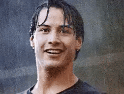 Celebrity gif. A young Keanu Reeves stands in the rain smiling. He raises up his arm and gives an enthusiastic thumbs up. (Added via Giphy)