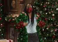 Tonight Show gif. A woman standing in front of a Christmas tree, in a den fully decked out in Christmas decor, turns to the left, then to the right, showing off her fully decked out Christmas sweater, complete with garland and ornaments that make her look like a Christmas tree.