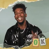 Celebrity gif. Desiigner grins and points up, flashing us an 