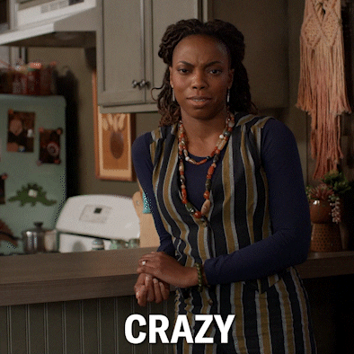 TV gif. Sasheer Zamata as Denise on Home Economics, leaning against a bar in a home kitchen, shaking her head and smiling as she says "crazy."