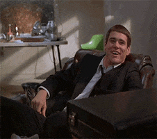Movie gif. Jim Carrey as Lloyd in Dumb and Dumber sits back in a chair. He looks up at someone and awkwardly laughs and shrugs, looking around the room as he continues to shrug.