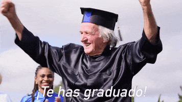 Video gif. Older man pumps his fists proudly in the air as he dons his black graduation cap and gown. In the background, others happily applaud for him. Text at the bottom reads, "¡Te has graduado!"