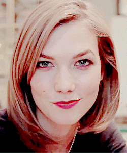 Celebrity gif. Karlie Kloss looks at us with a grin and slowly sticks her tongue out at us. 