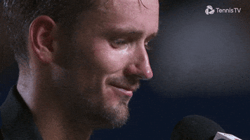Sports gif. Daniil Medvedev, a Russian tennis player, taps a microphone with one finger, smiling down and saying, "Hello," into the mic.