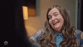 SNL gif. Aidy Bryant sits in a living room and smiles almost gleefully at someone off screen, nodding and gesticulating with her hands as she says, "Ouch but true." 