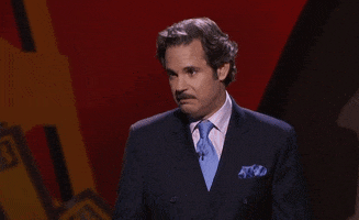 Celebrity gif. Wearing a dark blue suit with a light blue tie, Paul F. Tompkins recoils in disgust, then gives a playful thumbs-down.