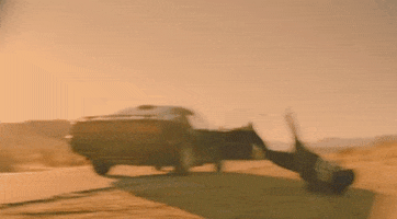 Music video gif. From the video for Sleigh Bells' Rill Rill, a man tumbles and rolls off the side of a dusty desert road while an old car continues down the road with the passenger door open.