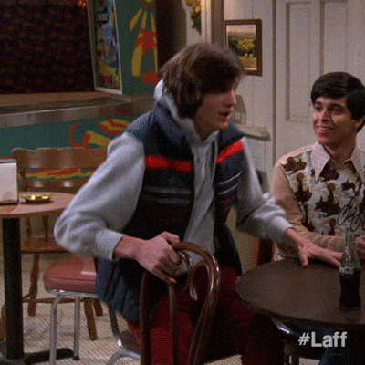 TV gif. Ashton Kutcher as Michael in That 70's Show jumps up from behind a round dining table, tossing his arms over his head with closed eyes and fists like he's overjoyed. Text, "Yes!"