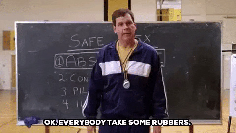 GIF of the sex education teacher from Mean Girls. He's holding out a box of condoms and saying, "Okay, everybody take some rubbers."