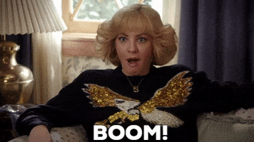 TV gif. Wendi McLendon-Covey as Beverly in The Goldbergs. She's lounging on a couch listening to good news and she yells, "BOOM," while clenching her fists and smiling, wide-mouthed.