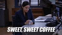 Gifs de televisão. Melissa Fumero como Amy Santiago em Brooklyn Nine Nine sentada em sua mesa e abrindo a tampa do café. Texto, "Café doce, doce."