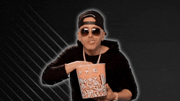 Celebrity gif. Yandel stuffs his mouth with popcorn as if captivated.