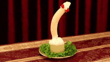 Video gif. A suggestive arrangement: a banana and two cherries dip repeatedly into some whipped cream and pineapple.