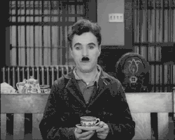 TV gif. Charlie Chaplin in Modern Times, sitting on a bench, tapping his finger on the saucer of a teacup and gazing off blankly.