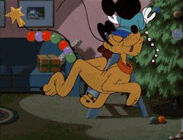 Disney gif. Pluto the dog proudly trots through a living room with Christmas decorations hanging from his tail. He stops and holds up his tail next to Mickey, who is decorating a Christmas tree. Mickey leans over and plucks the star from Pluto's tail.