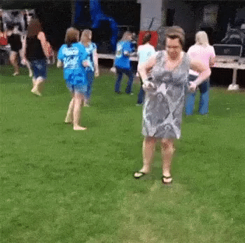 Video gif. A mom is at an outdoor party on the dance floor. She holds a drink in one hand and is dancing. She flails all her limbs up at different times and tries to find the groove, but fails, dancing awkwardly but with full passion.
