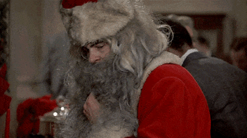 Movie gif. Dan Aykroyd as Louis in Trading Places wears a Santa suit, pulling down the beard to drink from a cocktail glass as he looks around anxiously.