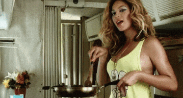 Celebrity gif. Beyonce is cooking in the kitchen and she holds a pan out while stirring it seductively.