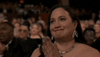 Oscars 2024 GIF. Lily Gladstone emotionally clasps her hands together in front of her face before she places her palms against her chest. 